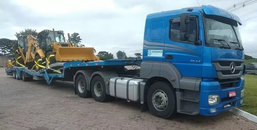 A foto mostra a carreta prancha da Bonança Transporte Nacional e Internacional de cargas transportando uma máquina da linha amarela