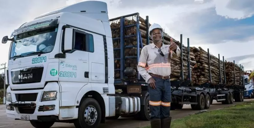 A foto mostra a carreta tritrem da empresa Eldorado Brasil e um funcionário fazendo sinal de jóia com o dedo