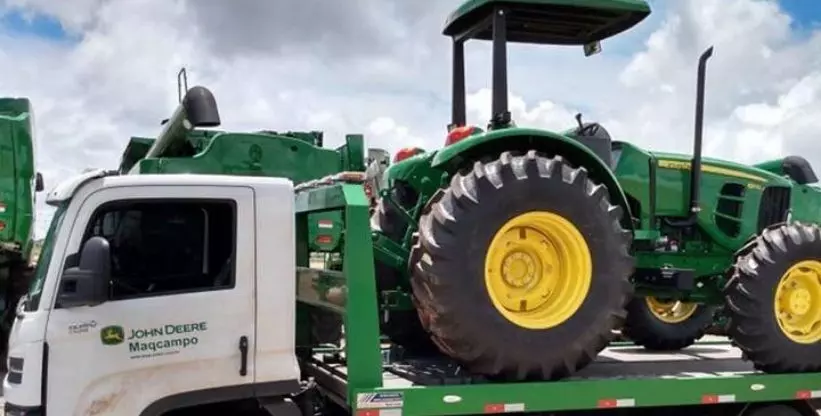A foto mostra um caminhão da Maqcampo - John Deere transportando um trator agrícola