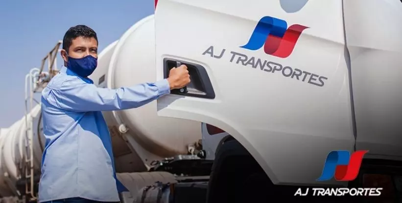 A foto mostra um motorista entrando em um caminhão da empresa AJ Transportes