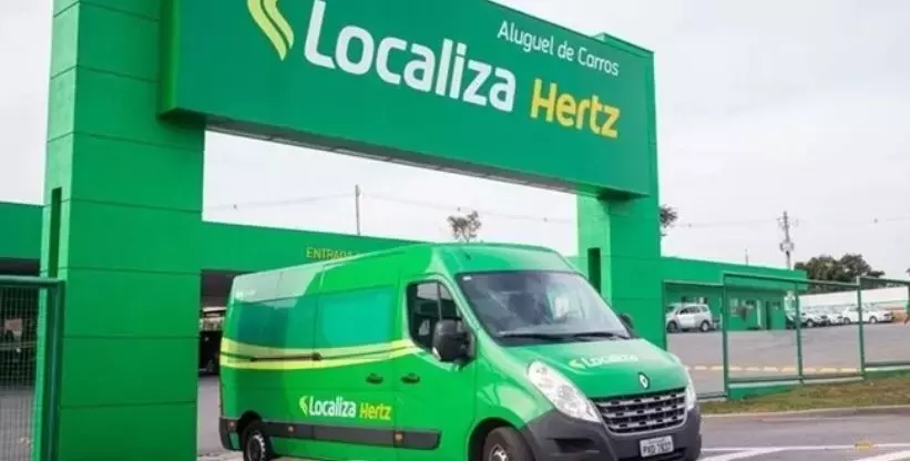 A foto mostra uma van da localiza saindo da agência Localiza